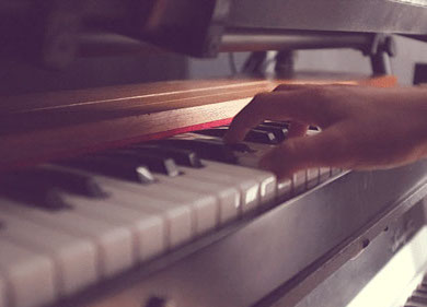 Photo couleur d'un personne qui joue un accord sur un piano vintage. Détail de la main et de l'instrument.